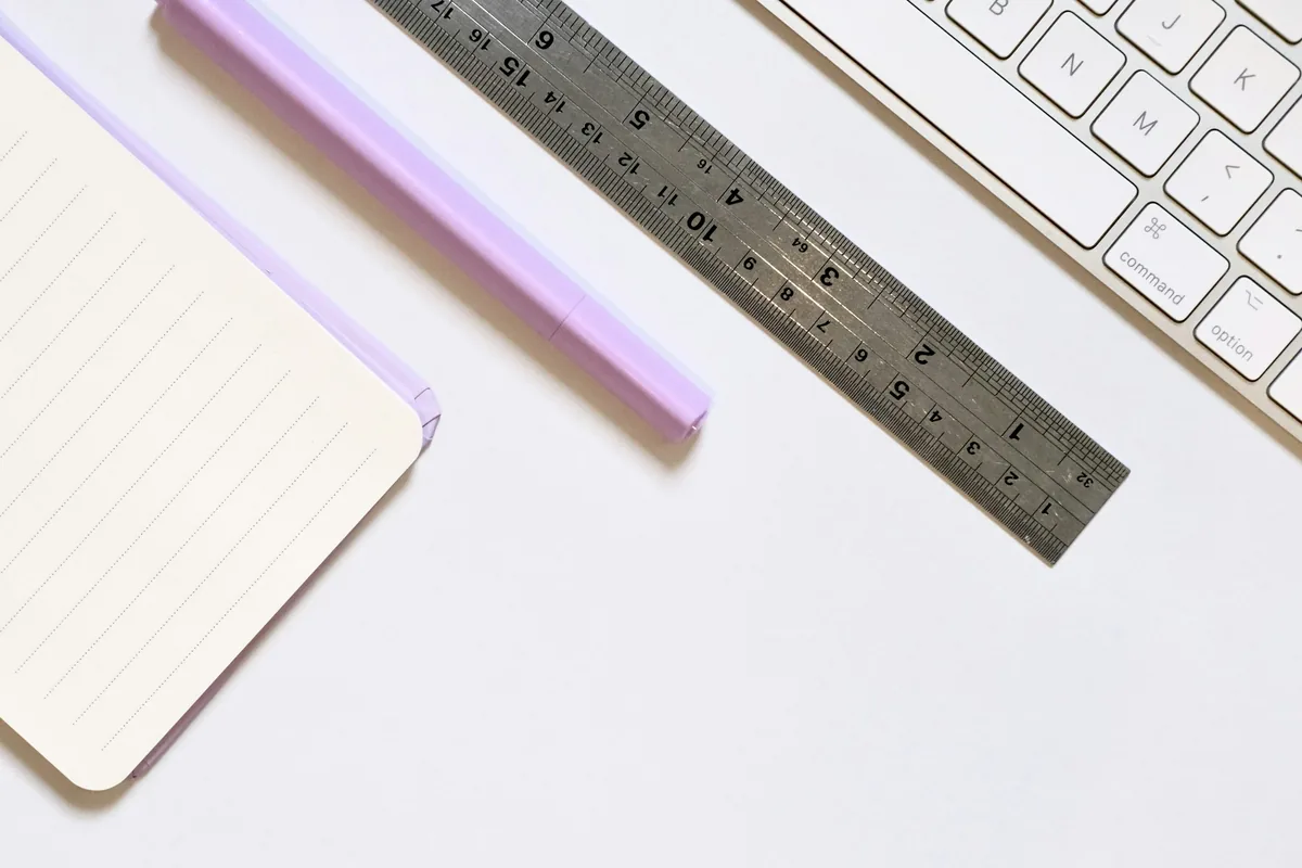 Illustrative stock photo of a blank notebook, purple pen, ruler and white computer keyboard.